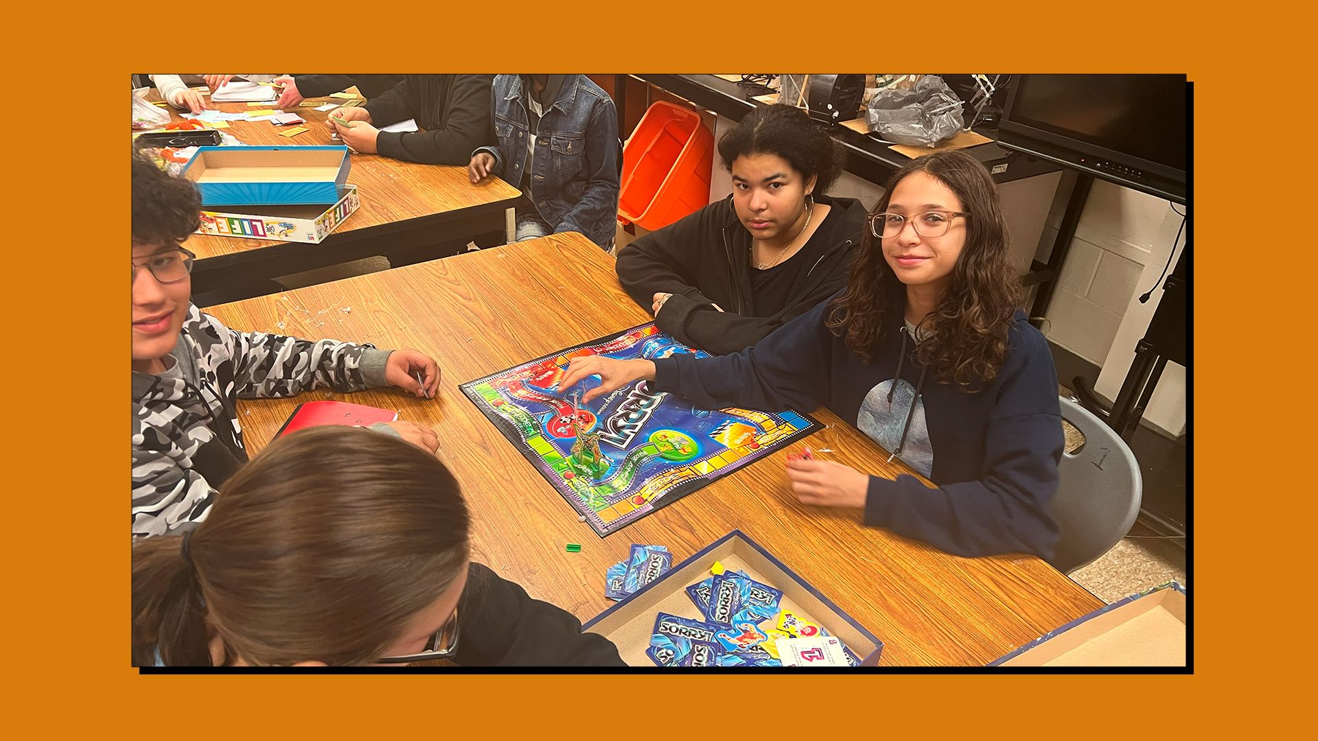 3 students playing the 'Sorry' board game and looking at the camera.